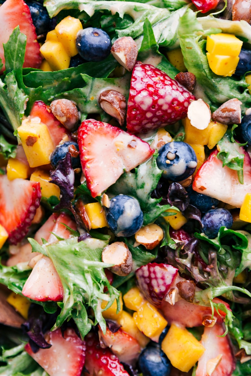 This delicious Mango Salad is loaded with fresh fruit, cinnamon almonds, and dressed with a cinnamon-yogurt dressing. Be prepared for a salad addiction! Recipe via ChelseasMessyApron.com #mangosalad #mango #berries #fruity #salad #cinnamonalmonds #almonds #cinnamon #yogurtdressing Overhead image of dish with the dressing coating everything.