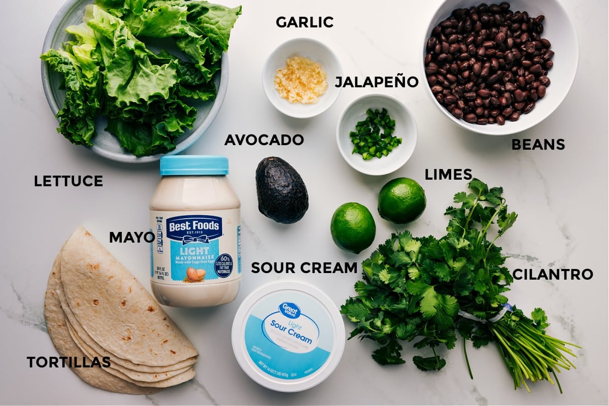 Ingredients In Black Bean Wraps All the ingredients for this recipe prepped and ready for easy assembly, including lettuce, avocado, limes, beans, sour cream, mayo, cilantro, and tortillas.