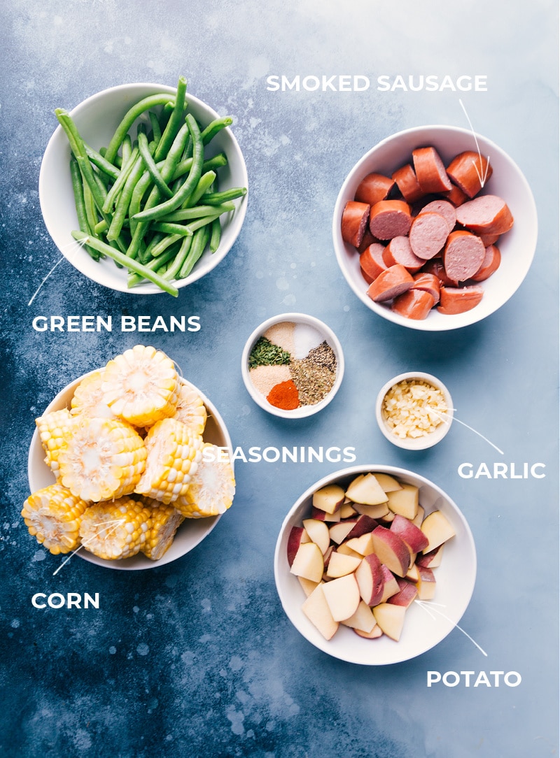 Easy Foil Pack Garlic Butter Sausage & Veggies with smoked sausage, red potatoes, sweet corn, and crisp green beans. These simple foil pack dinners can be prepped out in 15 minutes or less! Recipe via ChelseasMessyApron #dinner #quick #easy #simple #camping #overfire #grilled #garlicbutter #sausage #veggies #foilpacks Ingredient shot showing everything that goes into this meal