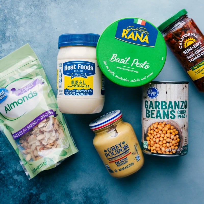 Ingredients In Pesto Chickpea Sandwiches Ingredients prepped for easy assembly, including pesto, tomatoes, mayo, almonds, garbanzo beans, and Dijon mustard.