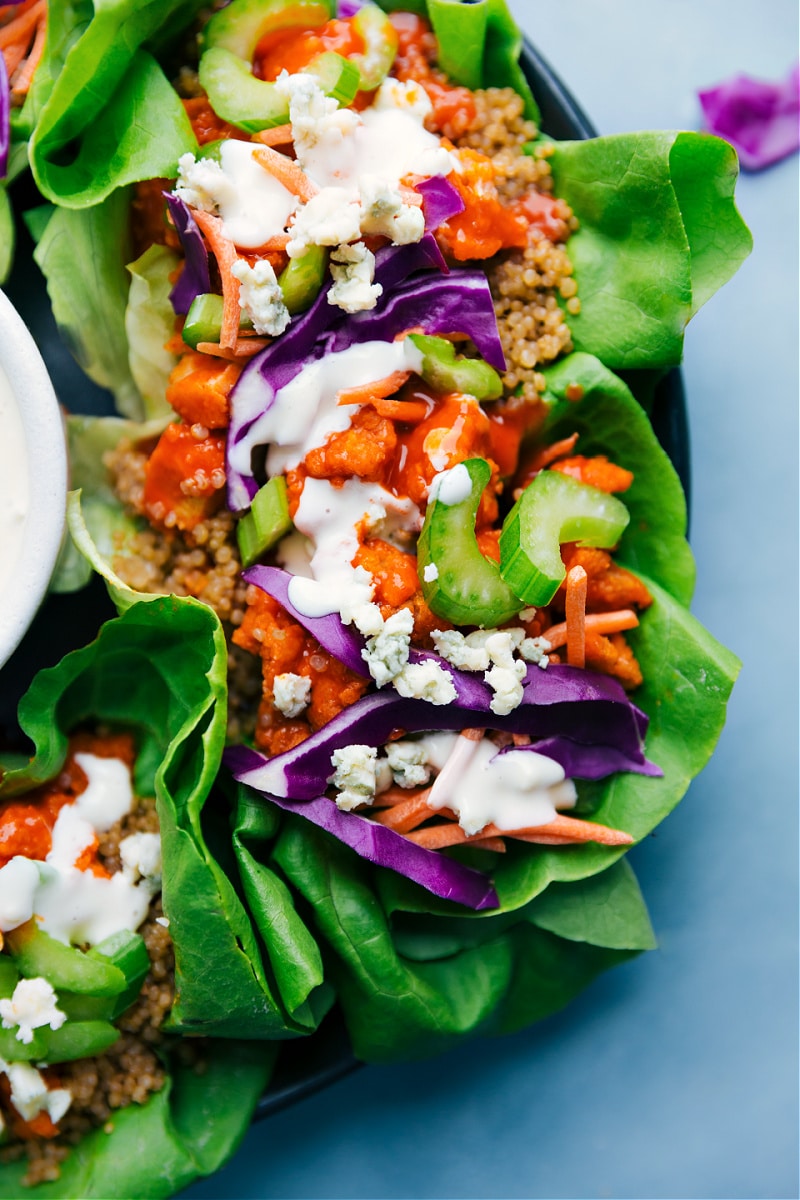 Buffalo Chicken Lettuce Wraps! Crispy chicken is tossed in buffalo sauce and loaded in crispy lettuce wraps, topped with crunchy veggies, and drizzled in a bold bleu cheese dressing. Recipe via ChelseasMessyApron #dinner #quick #easy #simple #spicy #sauce #quinoa #buffalo #chicken #lettuce #wraps Overhead image Buffalo Chicken Lettuce Wraps