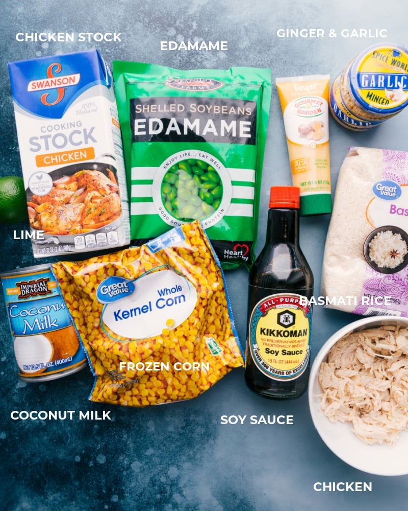 all the ingredients you need for this delicious meal Assembled ingredients, including chicken stock, edamame, ginger, garlic, lime, coconut milk, frozen corn, soy sauce, basmati rice, and cooked chicken.