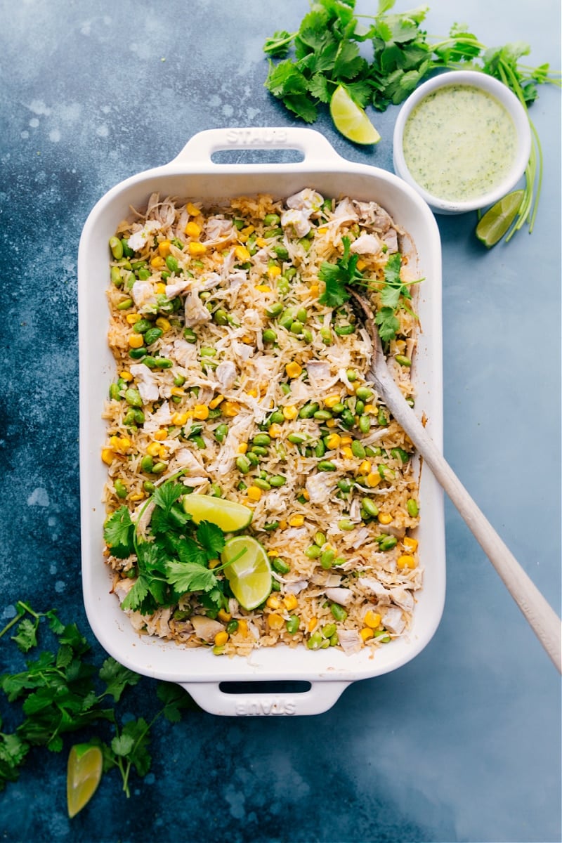 Coconut Chicken and Rice in a casserole dish with cilantro and lime wedges as a garnish.