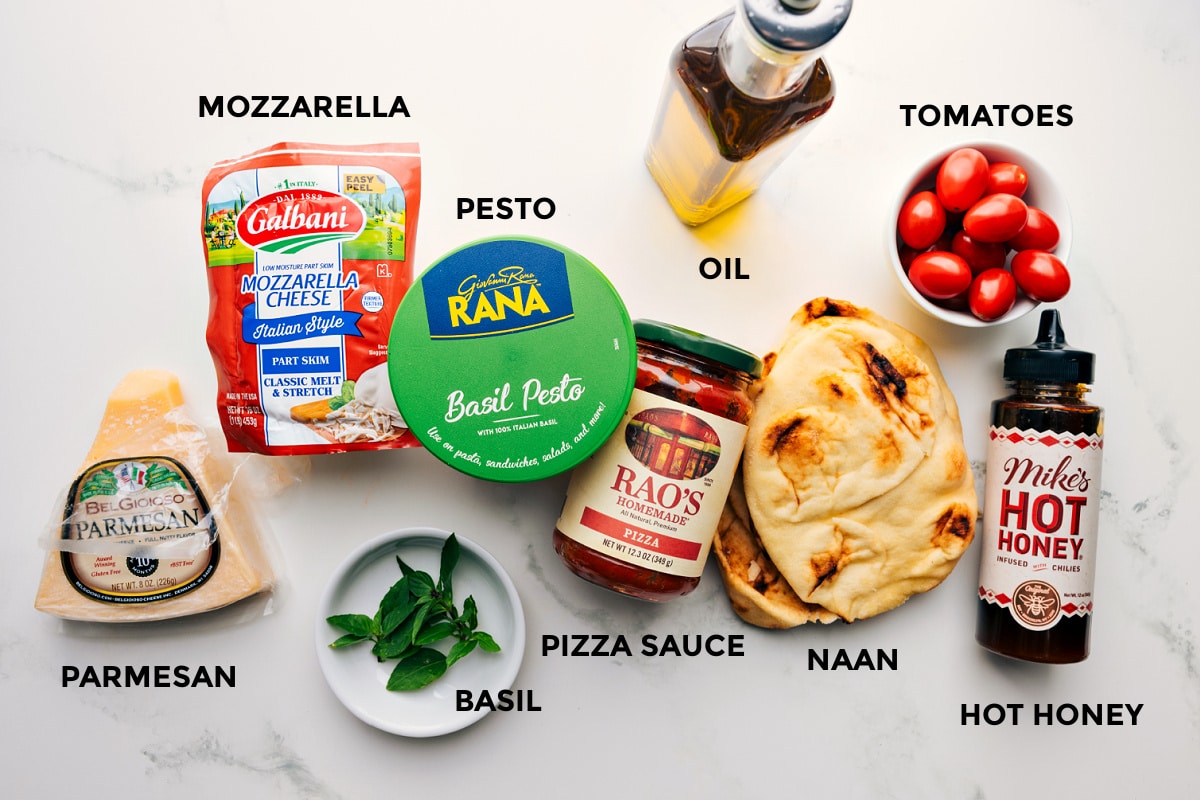 Ingredients In Naan Pizza All the ingredients prepped out for easy assembly including the parmesan, mozzarella, pesto, basil, sauce, oil, naan, hot honey, and tomatoes.