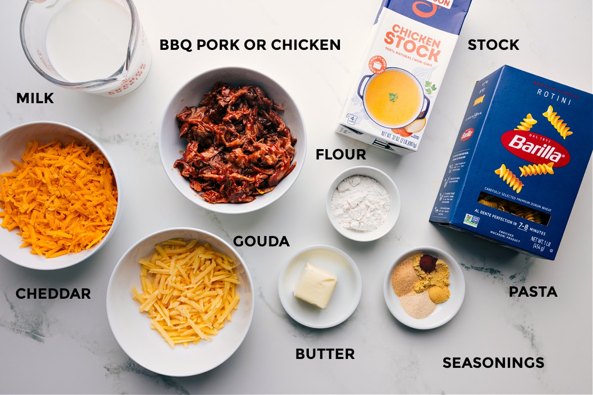 Ingredients In BBQ Mac And Cheese Recipe Ingredients prepped and ready for easy assembly: pork or chicken, milk, cheddar, gouda, flour, butter, seasonings, pasta, and stock.