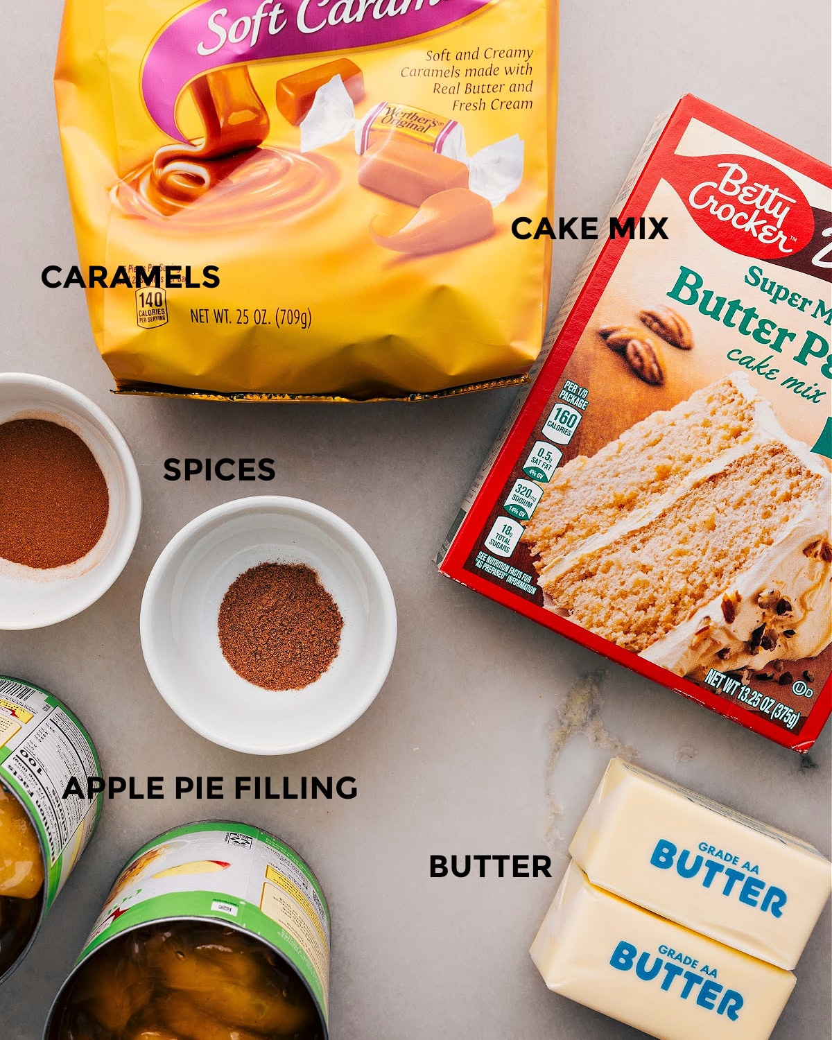 Apple Dump Cake Ingredients All the ingredients for this recipe are set out for easy assembly, including caramels, cake mix, spices, butter, and pie filling.