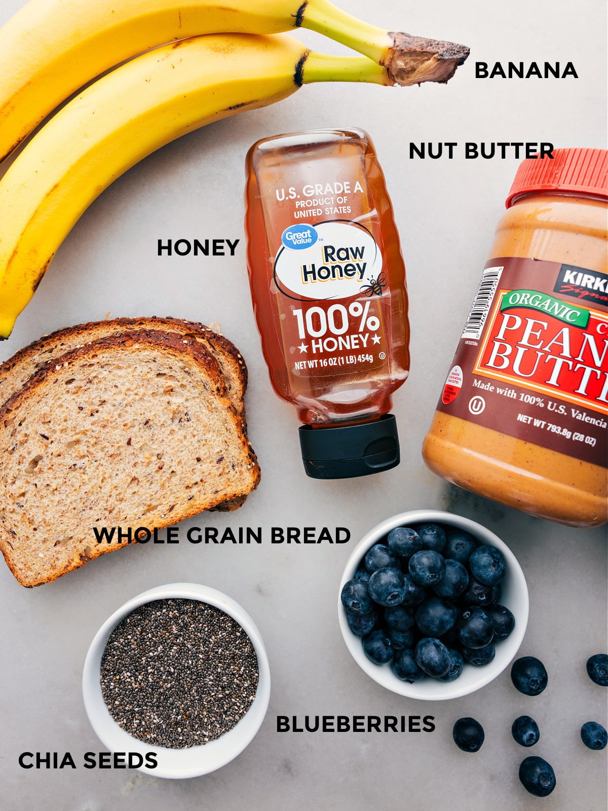 Ingredients In The Best Breakfast Toast All the ingredients like banana, nut butter, honey, whole grain bread, blueberries, and chia seeds prepped out for easy assembly.
