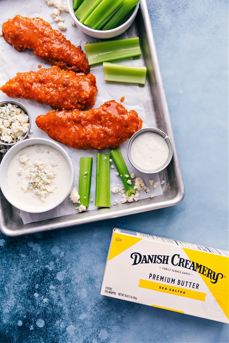 Our favorite Buffalo Chicken Tenders are baked to crispy perfection thanks to a few tricks in the preparation method. These baked tenders are an explosion of flavor and a good hit of spice. Dunk 'em in some blue cheese or ranch dressing and prepared to be hooked! Recipe via ChelseasMessyApron #dinner #quick #easy #simple #gameday #appetizer #spicy #buffalo #chicken #tenders Overhead image of the Buffalo Chicken Tenders