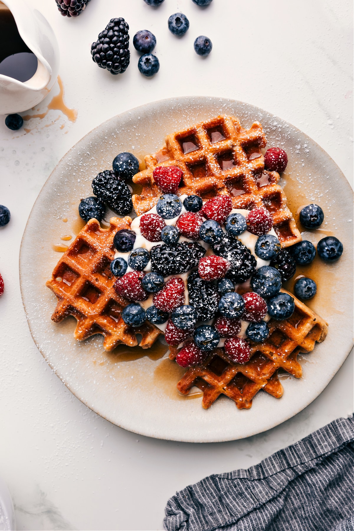 Healthy Waffle Recipe served with syrup, whipped cream, fresh berries, and powdered sugar.