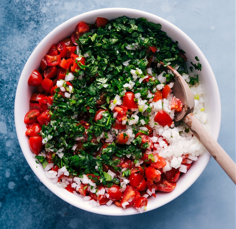 Pico de Gallo (also known as Salsa Fresca or Salsa Cruda) is made by combining diced tomatoes, onions, and peppers, with cilantro, lime juice, and salt.ย Recipe via ChelseasMessyApron #sidedish #best #quick #easy #dip #gameday #salsa #pico #degallo #healthy #cleaneating #wholefoods #picodegallo Overhead image of Pico de Gallo being tossed together