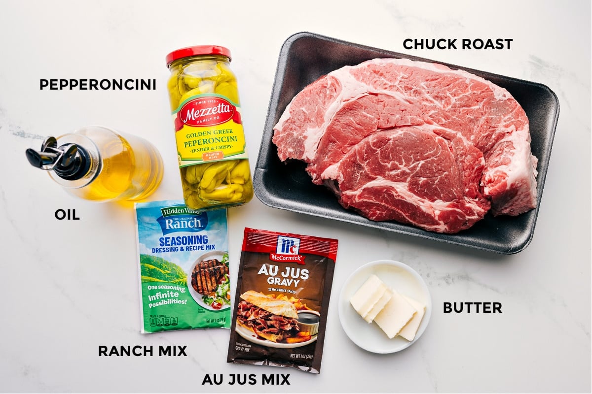Ingredients In Mississippi Pot Roast Recipe Ingredients prepped for easy assembly: pepperoncini, chuck roast, ranch mix, au jus mix, butter, and oil.