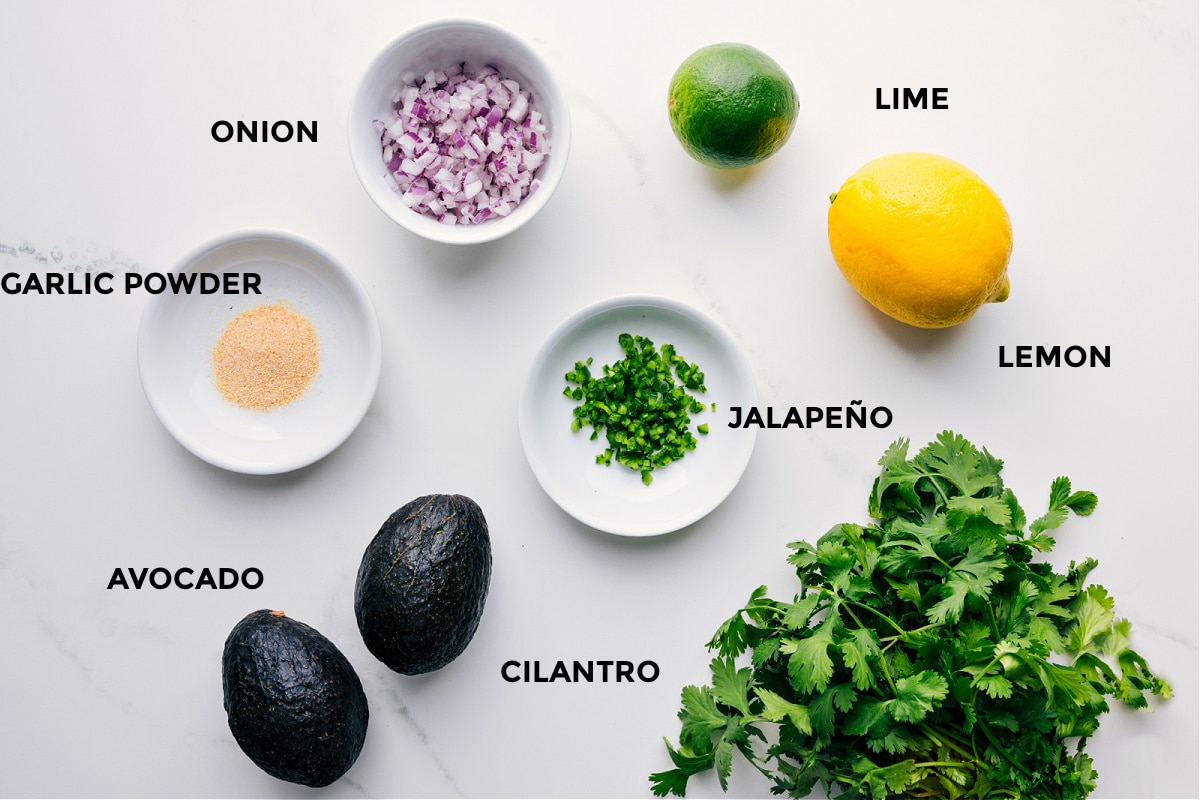 Ingredients In This Guacamole Recipe Ingredients prepped and ready, including onions, lime, lemon, jalapeรฑo, cilantro, avocado, and garlic powder.