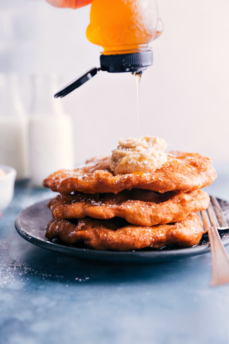Utah Scones are unlike scones anywhere else in the world! Unlike European scones that are served with clotted cream and tea or American biscuits, these scones are deep-fried pieces of a puffy flatbread that are enjoyed with a sprinkle of powdered sugar, honey, and butter. Recipe via ChelseasMessyApron #treat #dessert #best #quick #easy #simple #fried #frybread #utah #scones Image of honey being drizzled on the Utah Scones