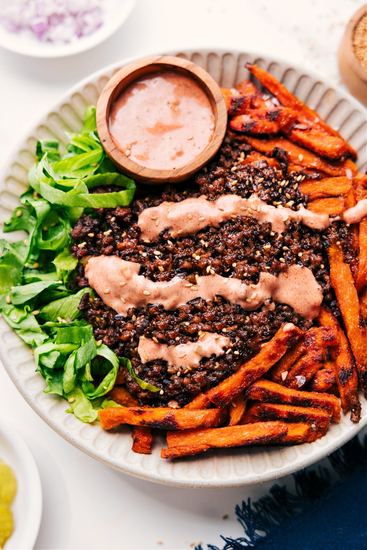 Burger Bowl with lettuce and sweet potato fries, topped with ground beef, burger sauce, and a sprinkle of sesame seeds.