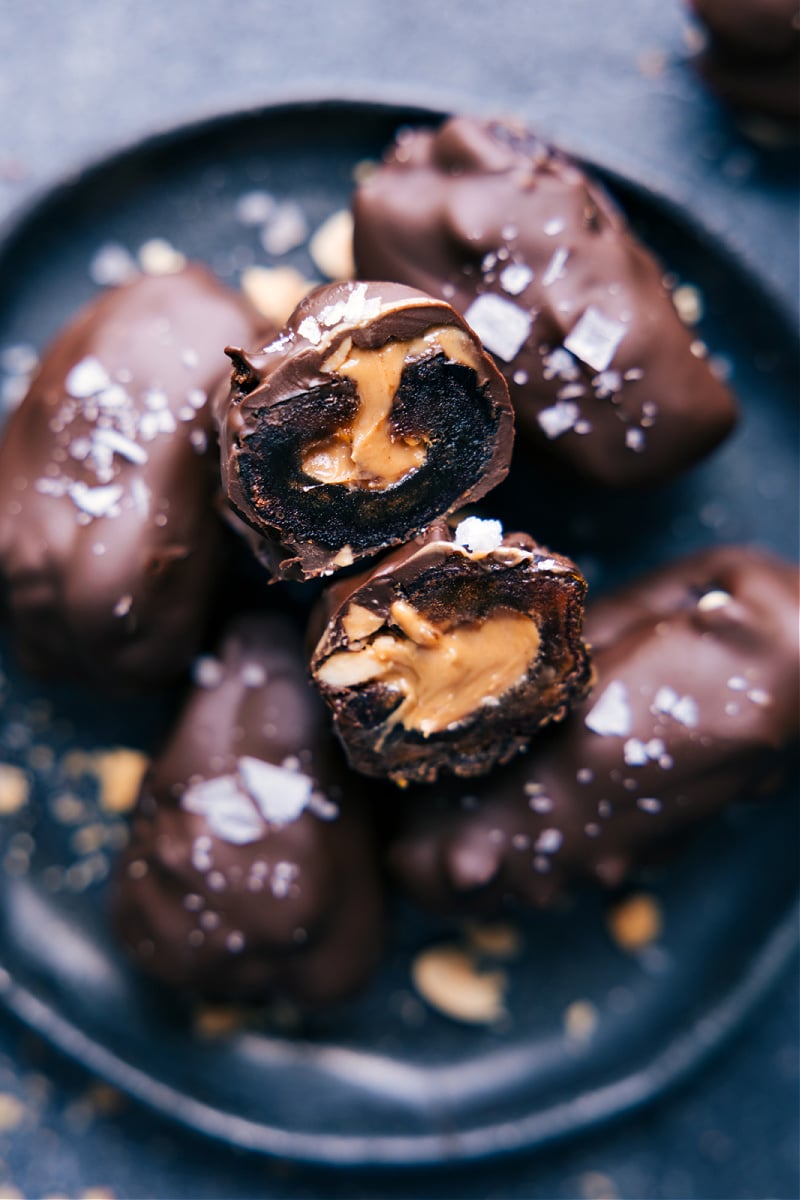 Chocolate Covered Dates make for the best snack, treat, or dessert. These indulgent-tasting treats are made with wholesome ingredients and are sure to cure your sweet tooth without any sugar hangover! Recipe via ChelseasMessyApron #snack #quick #easy #yummy #fresh #cleaneating #healthy #wholefoods #peanutbutter #chocolate #covered #dates The Chocolate Covered Dates on a plate with one cut open showing the nut butter inside.