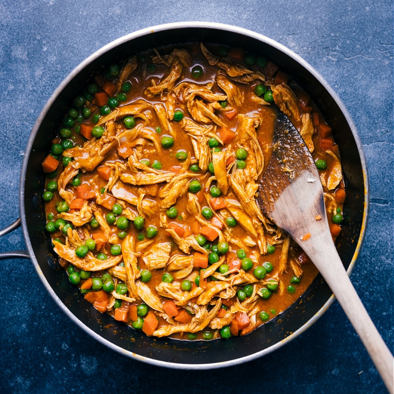 This simple and flavorful Garam Masala Chicken can be ready in 20 minutes or less. We combine chicken, peas, and carrots in a blend of spectacular spices and coconut milk. Recipe via ChelseasMessyApron.com #indian #garammasala #chicken #withrice #naan #coconutmilk #backtoschool Overhead view of Garam Masala Chicken in the pan