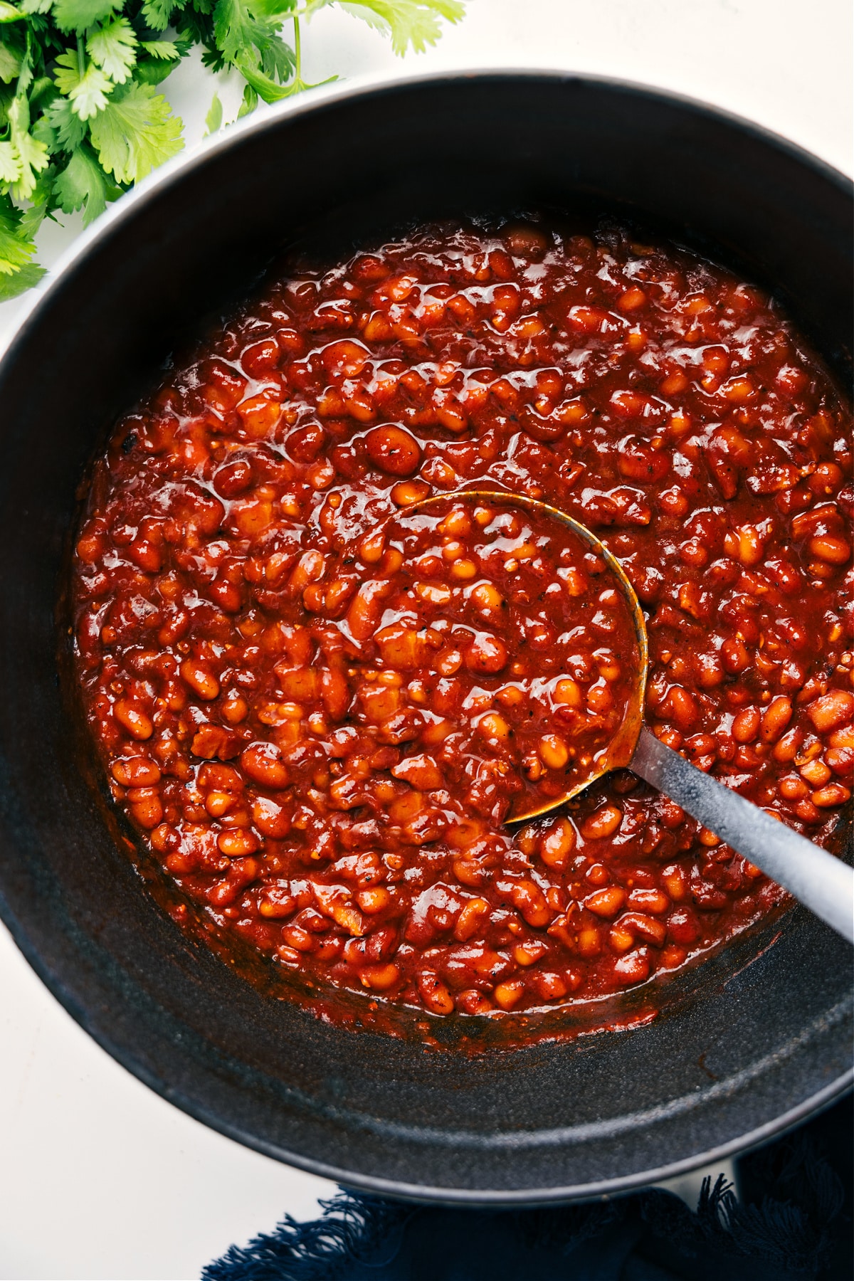 Baked Beans in a pot with a ladle lifting a hearty scoop.
