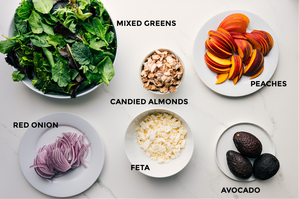 Ingredients In Peach Salad Ingredients in this recipe are prepped for easy assembly: mixed greens, red onions, feta, candied almonds, avocado, and peaches.