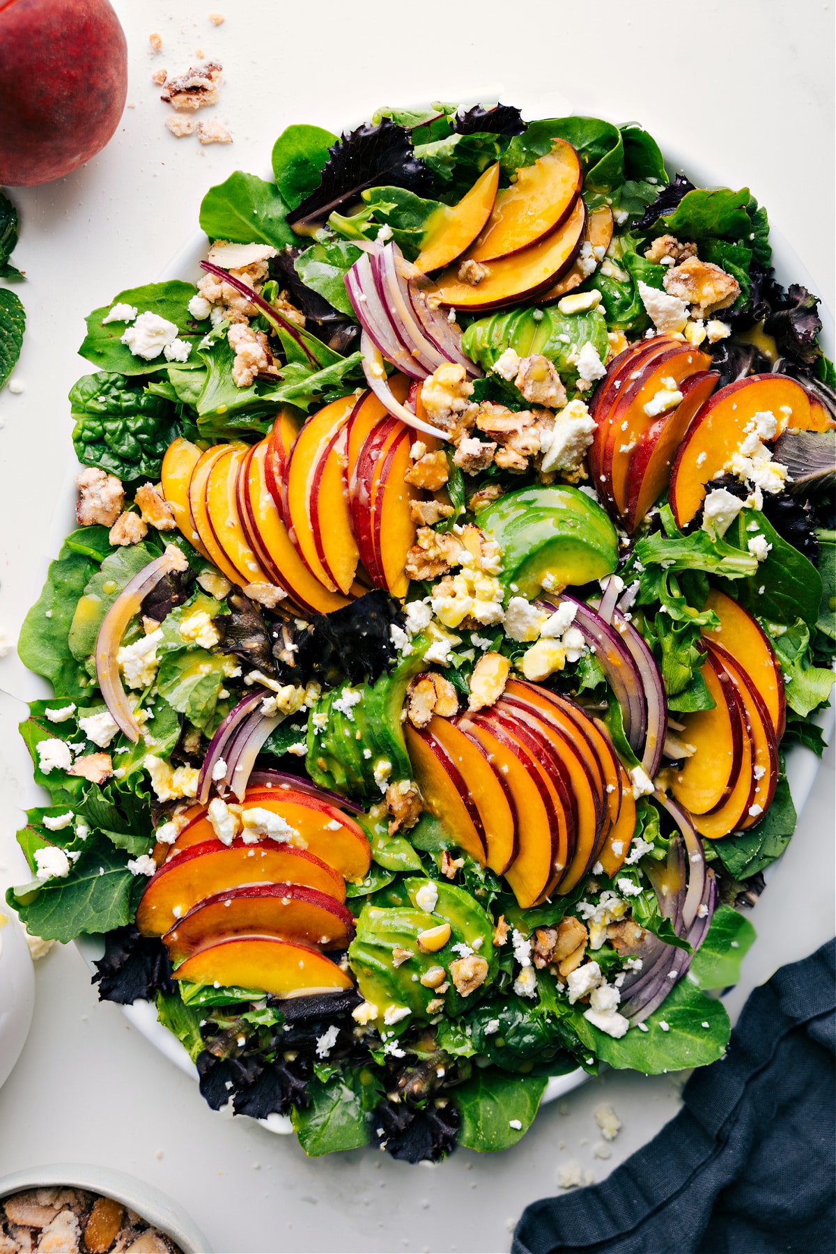 Fresh And Flavorful Peach Salad Recipe Peach salad with fresh peaches, red onions, feta, and candied almonds over lettuce, drizzled with dressing.