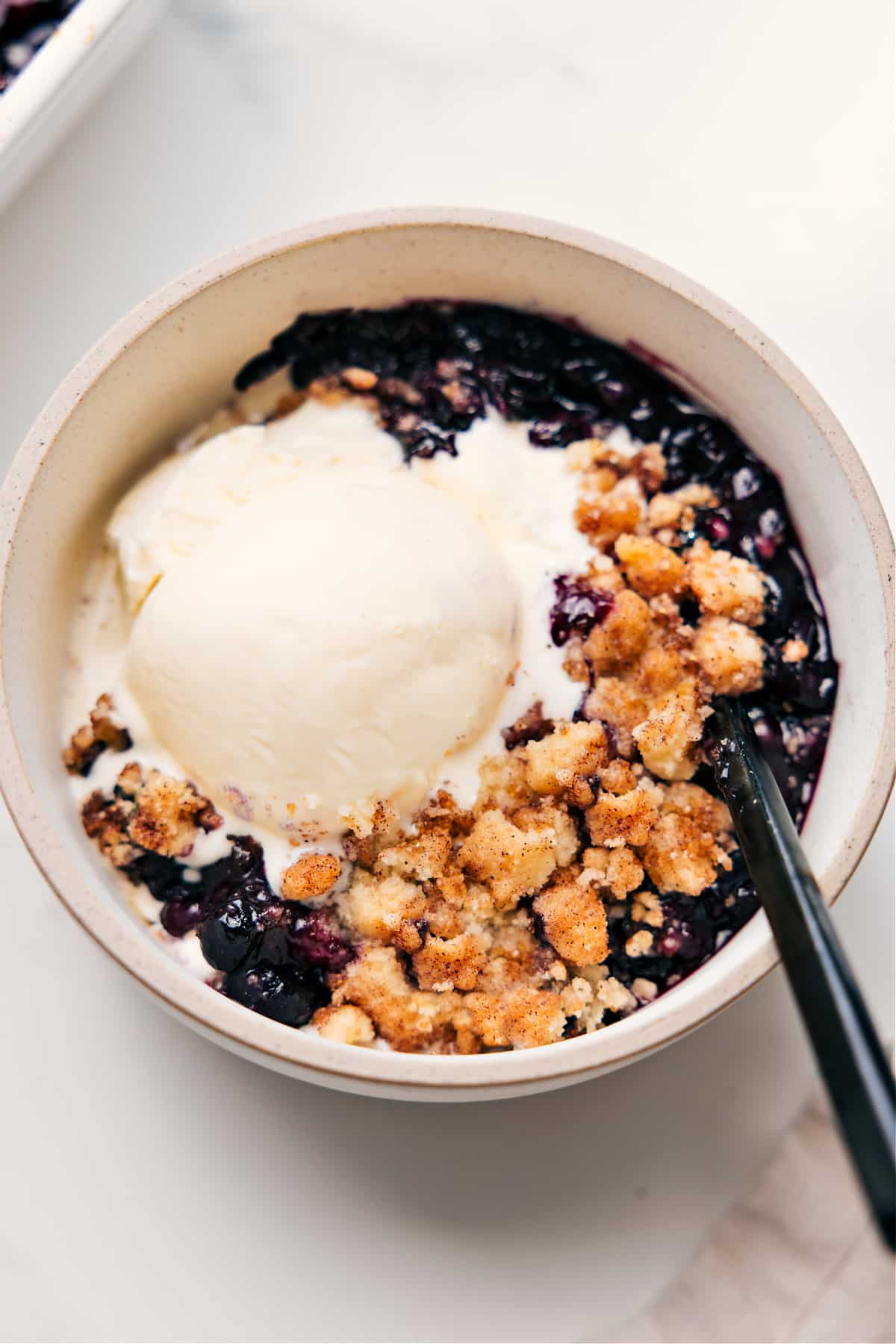 Blueberry Cobbler Recipe served in a bowl with a scoop of vanilla ice cream on top.