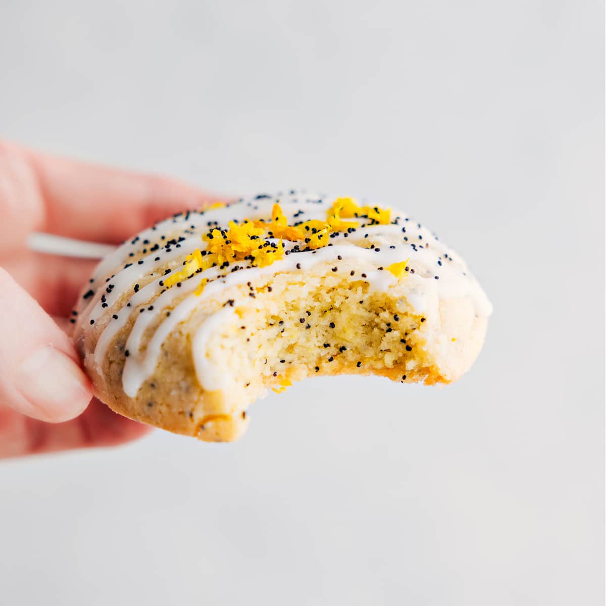 Delicious And Flavorful Lemon Poppy Seed Cookie Recipe The treat with a glaze and fresh lemon zest on top with a bite out of it.