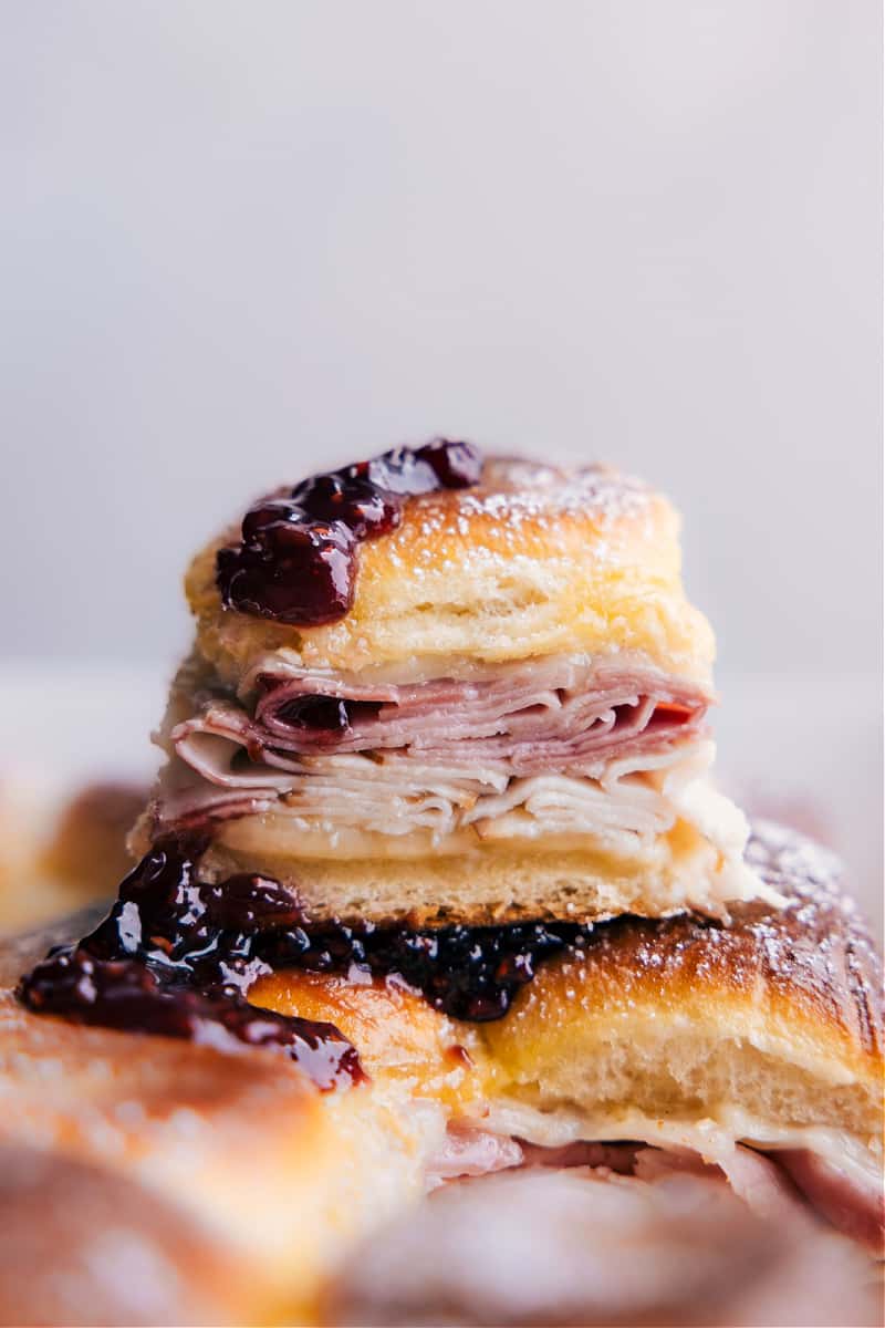 Monte Cristo Sliders are an easier take on the famous Monte Cristo Sandwich! Sweet Hawaiian rolls are layered with an irresistible Dijon-butter sauce and piled high with Swiss cheese, honey ham, and smoked turkey. These sliders are baked in an egg custard, topped with powdered sugar, and served with berry jam -- swoon! Recipe via ChelseasMessyApron #dinner #quick #easy #simple #best #fresh #lunch #familyfriendly #kidfriendly #jam #powderedsugar #monte #cristo #montecristo #sliders Image of the Monte Cristo sliders Stacked on top of each other