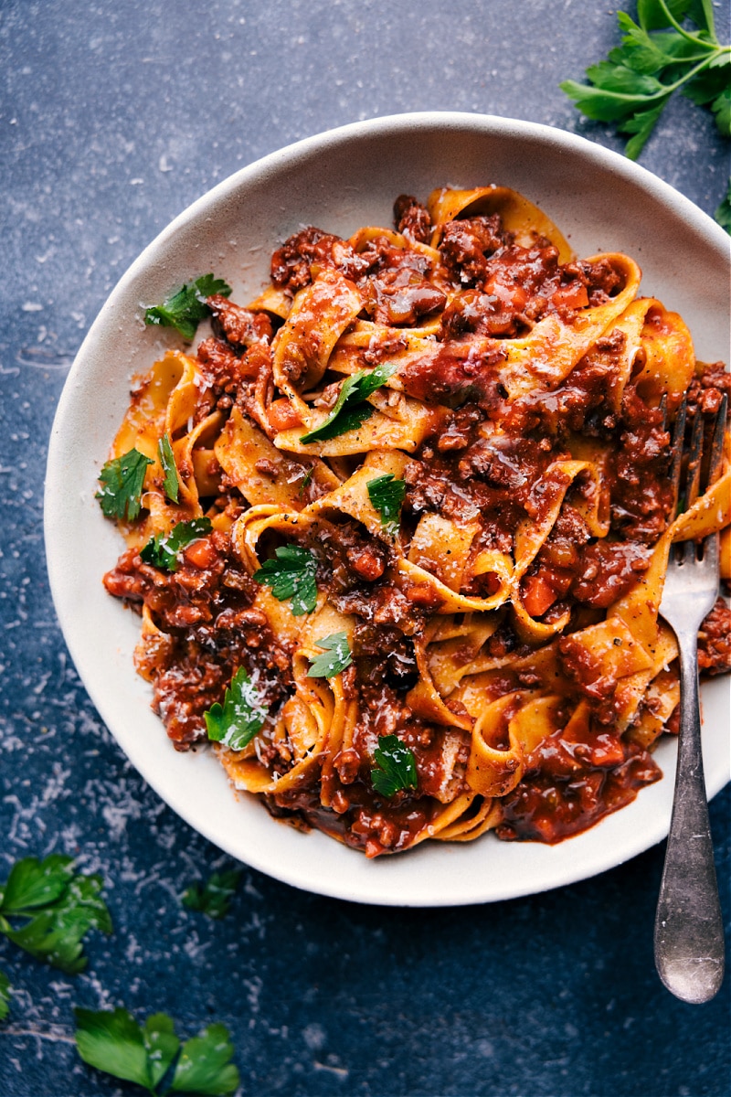 This rich Ragu sauce combines ground beef and Italian sausage with diced veggies and crushed tomatoes. This deeply savory and indulgent-tasting sauce gets tossed with pasta, garnished with herbs, and topped with freshly grated Parmesan. Recipe via chelseasmessyapron #dinner #quick #easy #simple #best #familyfriendly #kidfriendly #groundbeef #comfortfood #ragu Overhead image of the best Ragu