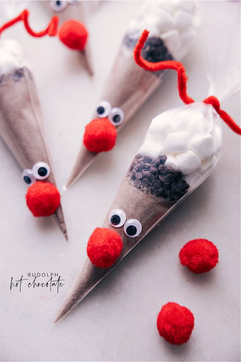 Reindeer Hot Chocolate -- the cutest edible gift this holiday season! Add hot chocolate mix, chocolate chips, and marshmallows to a cone-shaped bag and decorate to look like Reindeer (specifically Rudolph). Put a smile on your kid's face or gift out to neighbors, friends, co-workers, family, etc. Recipe via chelseasmessyapron #dessert #gift #christmas #holidays #christmasgifts #holidaygifts #rudolph #reindeer #hot #chocolate Overhead image of Reindeer Hot Chocolate