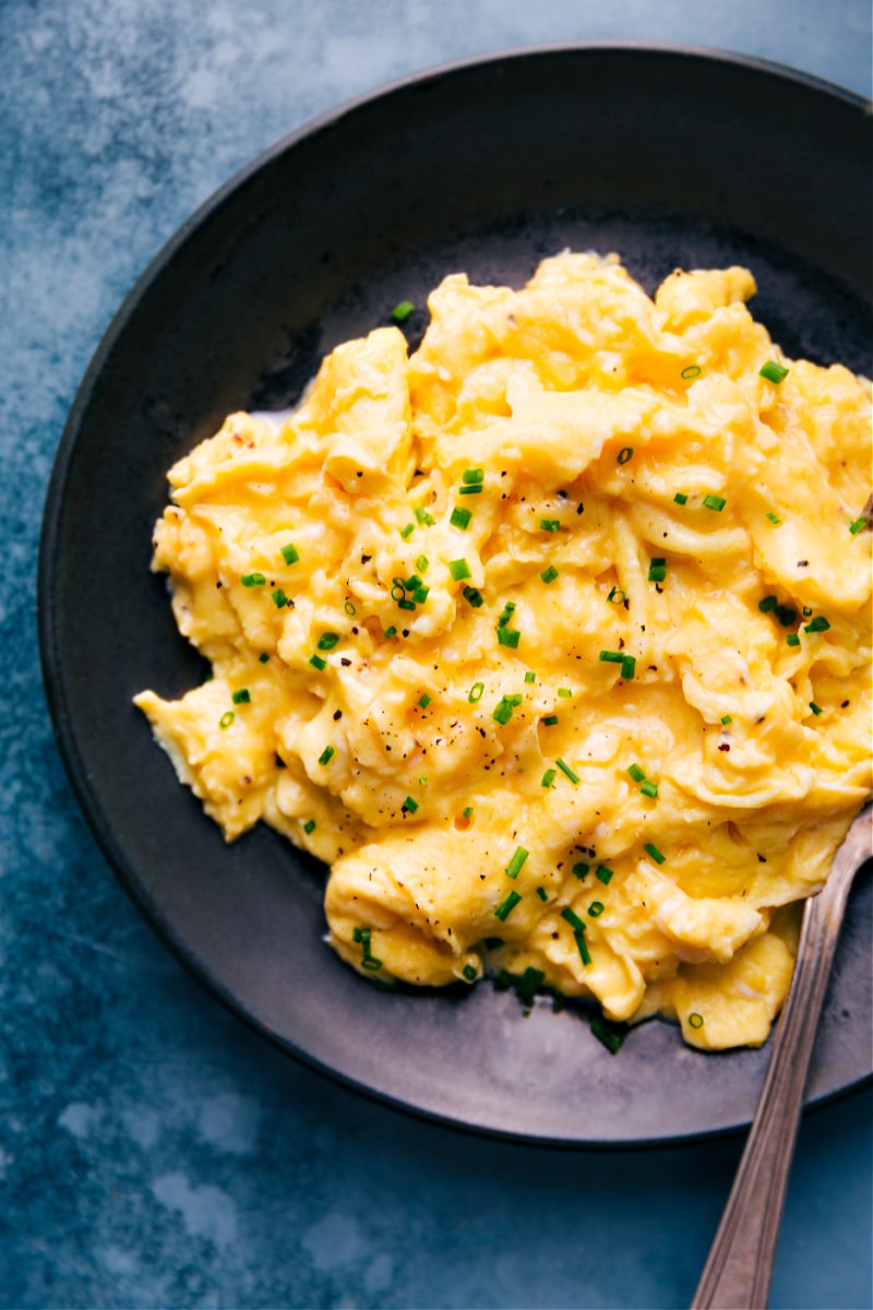 This delicious recipe for Scrambled Eggs will elevate your breakfast game with its easy to follow steps, simple ingredients, and a technique that guarantees a delicious, creamy, and custardy pile of eggs every time. Get ready for a breakfast that will have everyone at the table asking for seconds! Recipe via chelseasmessyapron #sidedish #best #quick #easy #simple #breakfast #brunch #healthy #scrambled #eggs Up-close overhead image of the breakfast