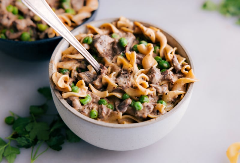 Treat yourself to the ultimate comfort food with this delightful Beef and Noodles recipe. It boasts juicy, tender beef and sweet peas, bathed in a luxuriously rich and flavorful sauce. Enjoy the epitome of coziness, served over egg noodles or mashed potatoes--it's a satisfying meal that you'll crave again and again. Recipe via ChelseasMessyApron.com #beefandnoodles #beef #noodles #chuckroast #roast #creamy #comfortfood #mashedpotatoes #instantpot #slowcooker #crockpot Bowl of saucy noodles and beef with a fork digging in