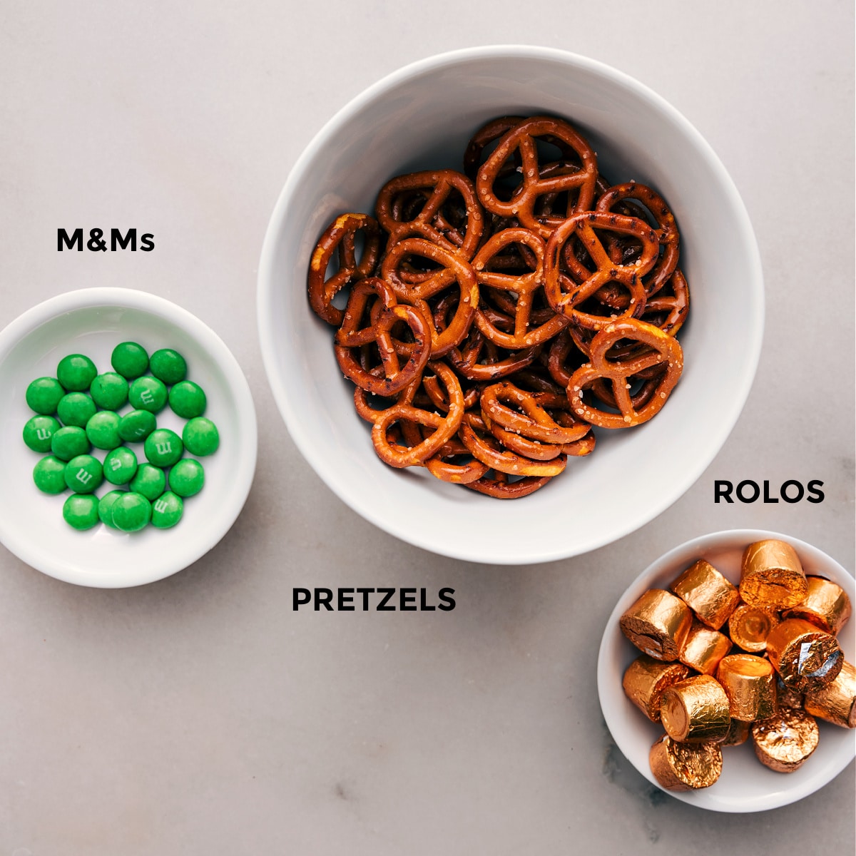 Ingredients In Leprechaun Thumbprints The 3 simple ingredients—M&Ms, pretzels, and Rolos—are prepped for easy assembly.