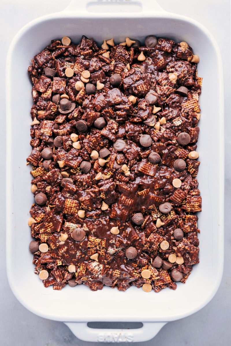 Muddy Buddy Bars! This recipe starts with crispy Chex cereal, which is coated in a delicious blend of creamy, chocolatey, and peanut buttery goodness. The best part? These bars are incredibly simple to make and require no baking. Recipe via chelseasmessyapron #dessert #best #quick #easy #simple #treat #snack #nobake #muddybuddy #bars Overhead image of the bars being pressed into the 9x13-inch pan
