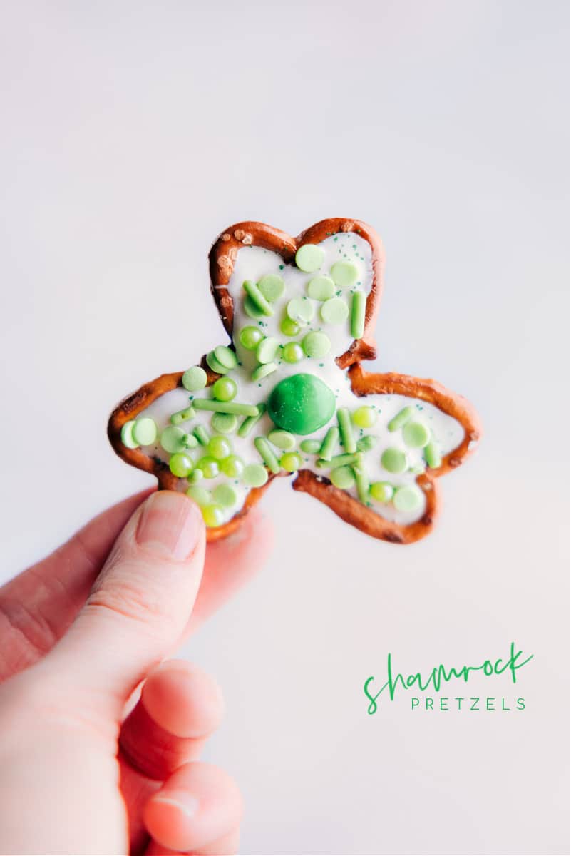 Transform a few simple ingredients into some downright delicious Pretzel Shamrocks -- perfect for St. Patrick's Day! These shamrocks double as both a sweet treat and cute table decor. Whether you're looking for a fun activity to do with the kids or a last-minute party snack, these Pretzel Shamrocks are the perfect thing to make! Recipe via chelseasmessyapron #dessert #best #quick #easy #simple #familyfriendly #stpatricksdays #stpatricks #pretzel #shamrocks Pretzel Shamrocks being held up.