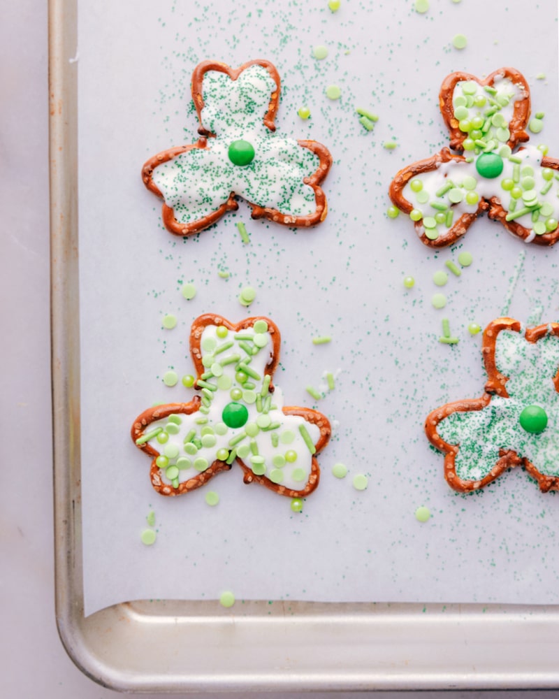 Transform a few simple ingredients into some downright delicious Pretzel Shamrocks! These shamrocks double as both a sweet treat and cute table decor. Whether you're looking for a fun activity to do with the kids or a last-minute party snack, these Pretzel Shamrocks are the perfect thing to make! Recipe via chelseasmessyapron #dessert #best #quick #easy #simple #familyfriendly #stpatricksdays #stpatricks #pretzel #shamrocks Overhead image of Pretzel Shamrocks on a tray