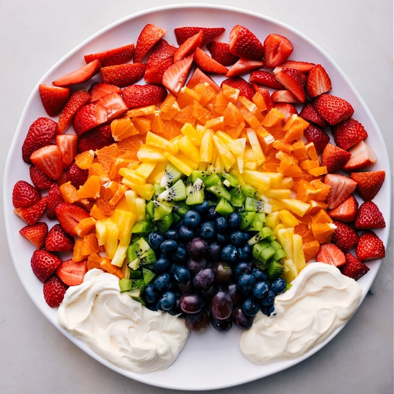 You've got to try this delicious Fruit Rainbow Tray with a quick, 3-ingredient Fruit Dip! Perfect for parties, family gatherings, or just a fun snack, this vibrant and delicious tray is sure to brighten up any occasion. Featuring a colorful array of fresh fruits arranged to resemble a rainbow, and a creamy and decadent fruit dip, this recipe is as fun to look at as it is to eat. Recipe via chelseasmessyapron #dessert #best #quick #easy #simple #healthy #wholefoods #cleaneating #fruitdip #dip #fruitraiinbow #tray Overhead image of the Rainbow Fruit Tray ready to be enjoyed