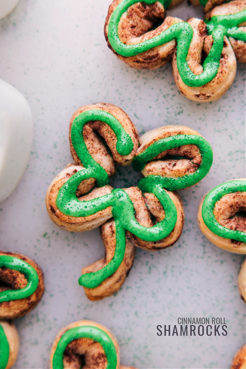 St. Patrick's Day is just around the corner! These adorable treats are not only festive and fun, but they're also incredibly easy to make. With just a can of refrigerated cinnamon rolls and some green food coloring, you can transform a classic breakfast pastry into a holiday masterpiece that kids and adults alike will love! Recipe via ChelseasMessyApron.com #cinnamonrolls #breakfast #shamrock #Stpatricksday #holiday #treat Overhead view of several iced Shamrock Cinnamon Rolls