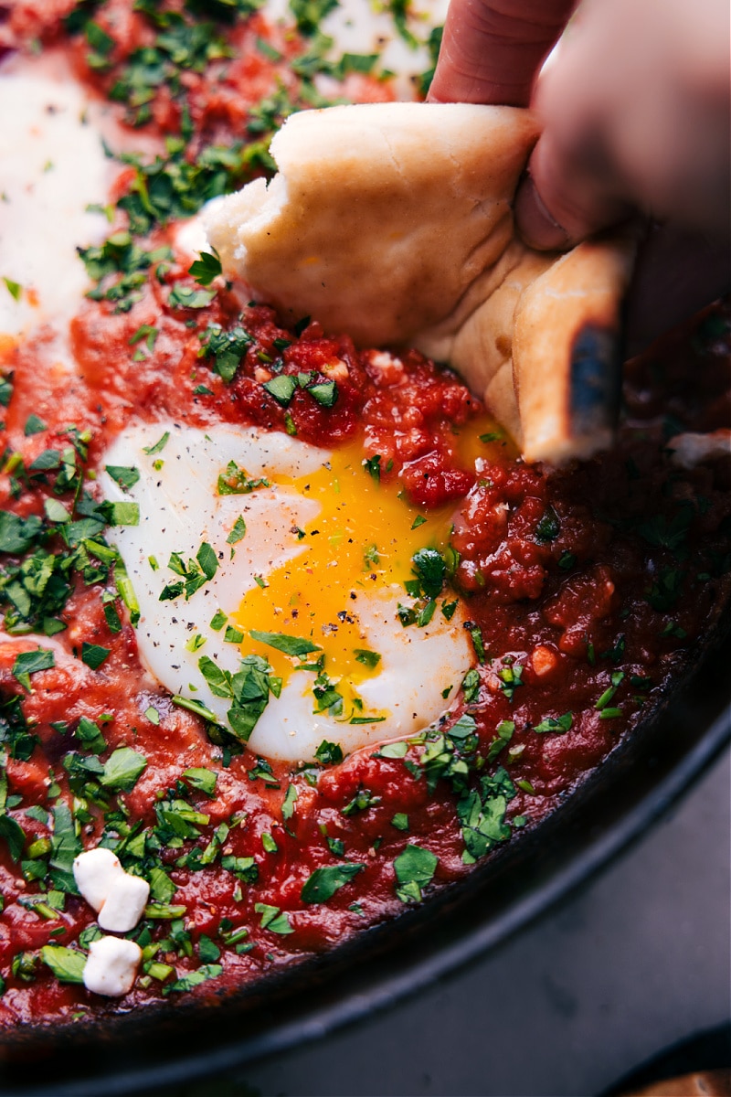Are you tired of the same old boring breakfast routine? Spice things up with Shakshuka, a vibrant and delicious dish that has become a staple of Middle Eastern and Mediterranean cuisine. Picture this: a bubbling, spicy tomato sauce infused with spices and garlic, with perfectly poached eggs nestled on top, all waiting to be devoured with warm, crusty bread or pita. Recipe via chelseasmessyapron #breakfast #quick #easy #simple #best #brunch #healthy #shakshuka Overhead image of Shakshuka