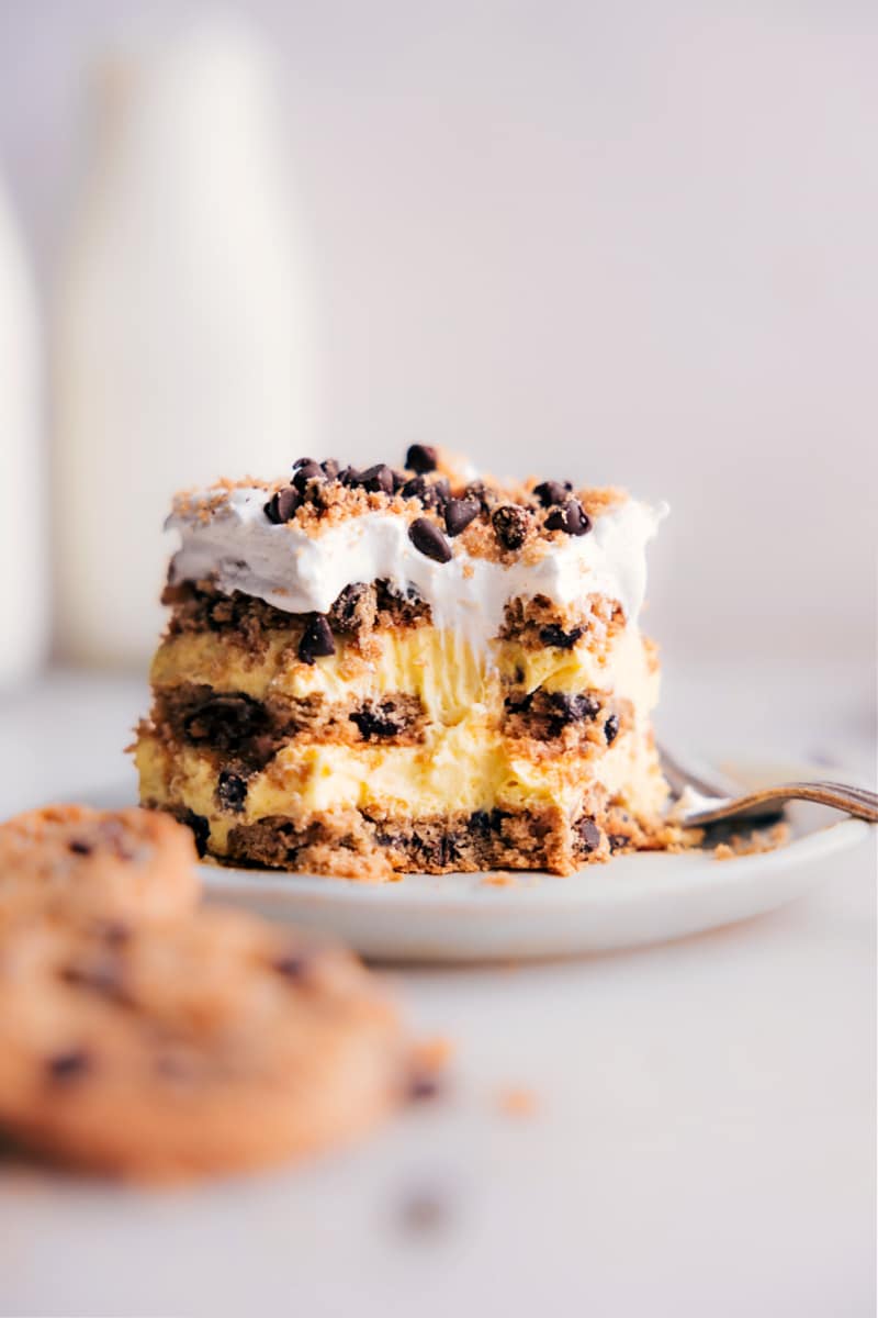 Looking for an impressive dessert that won't take hours in the kitchen? Then, you've got to try this Chocolate Chip Cookie Icebox Cake! Recipe via chelseasmessyapron #dessert #best #quick #easy #simple #familyfriendly #kidfriendly #chocolatechip #cookie #iceboxcake image of a slice of the Chocolate Chip Cookie Icebox Cake on a plate with a bite out of it