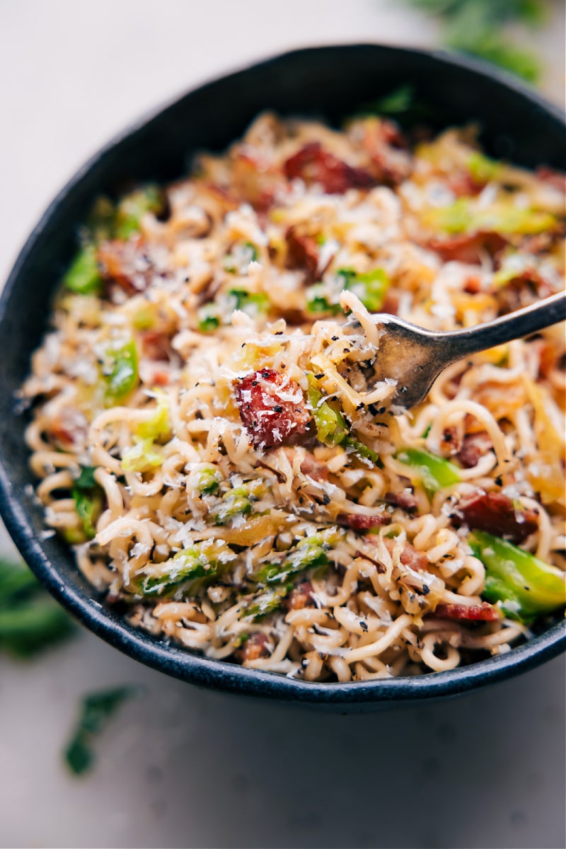 Our favorite Fried Cabbage Ramen recipe! With the addition of smoky bacon, savory onions, and salty parmesan cheese, these noodles are bursting with flavor. This jazzed-up ramen will quickly become a new favorite in your recipe collection! Recipe via chelseasmessyapron #dinner #quick #easy #simple #noodles #asian #stirfry #fried #cabbage #ramen Image of a fork full of the dish coming out of a bowl
