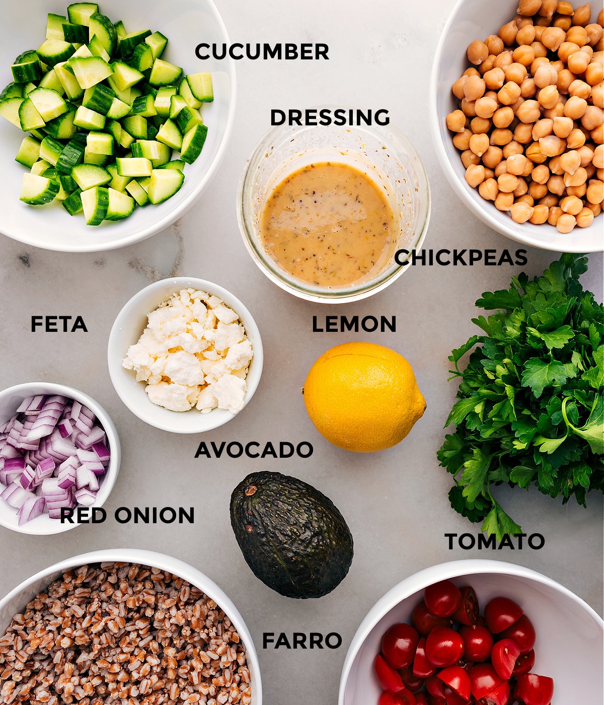 Ingredients In This Grain Bowl Recipe This recipe includes prepped ingredients like dressing, chickpeas, veggies, feta, lemon, farro, and parsley for easy assembly.