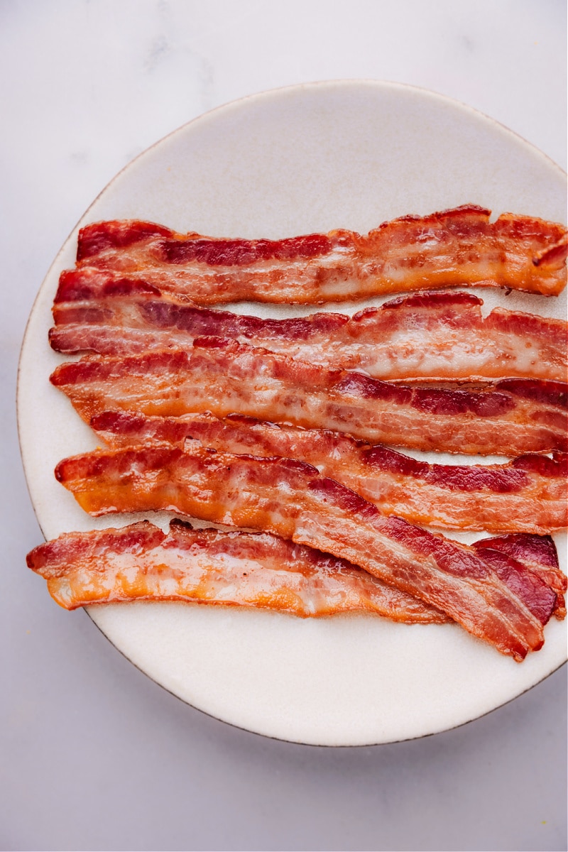 Bacon is crispy, savory, and deliciously salty, and can be served in a variety of ways. While most people fry their bacon on the stove, baking it is actually a great alternative that yields perfect results every time. Today, weโll provide you with a step-by-step guide on How To Bake Bacon to perfection! Recipe via chelseasmessyapron #sidedish #breakfast #best #quick #easy #simple #brunch #onepan #howtobake #bacon Overhead image of the breakfast on a plate ready to be enjoyed