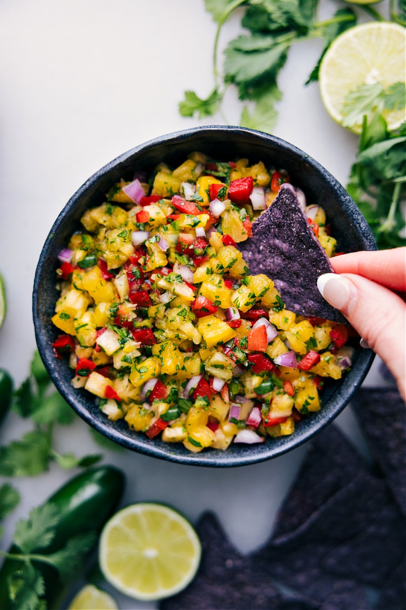 The Tastiest Pineapple Salsa Dipping a tortitlla chip into pineapple salsa in a bowl.