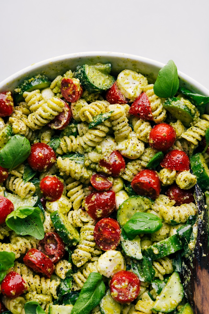 This delicious Pesto Pasta Salad combines rotini pasta, juicy cherry tomatoes, crisp cucumbers, and creamy mozzarella pearls, all tossed in a luscious, herbaceous basil pesto dressing. The creamy dressing is what takes this salad to the next level, with its tangy notes of mayo, sour cream, and dijon mustard, perfectly balanced by the bright, zesty flavor of fresh basil-pesto and lemon juice. This salad is easy to make and sure to be a hit wherever it's served! Recipe via chelseasmessyapron #dinner #quick #easy #simple #familyfriendly #kidfriendly #sidedish #noodles #bbq #pesto #pastasalad Up-close overhead image of the Pesto Pasta Salad ready to be enjoyed