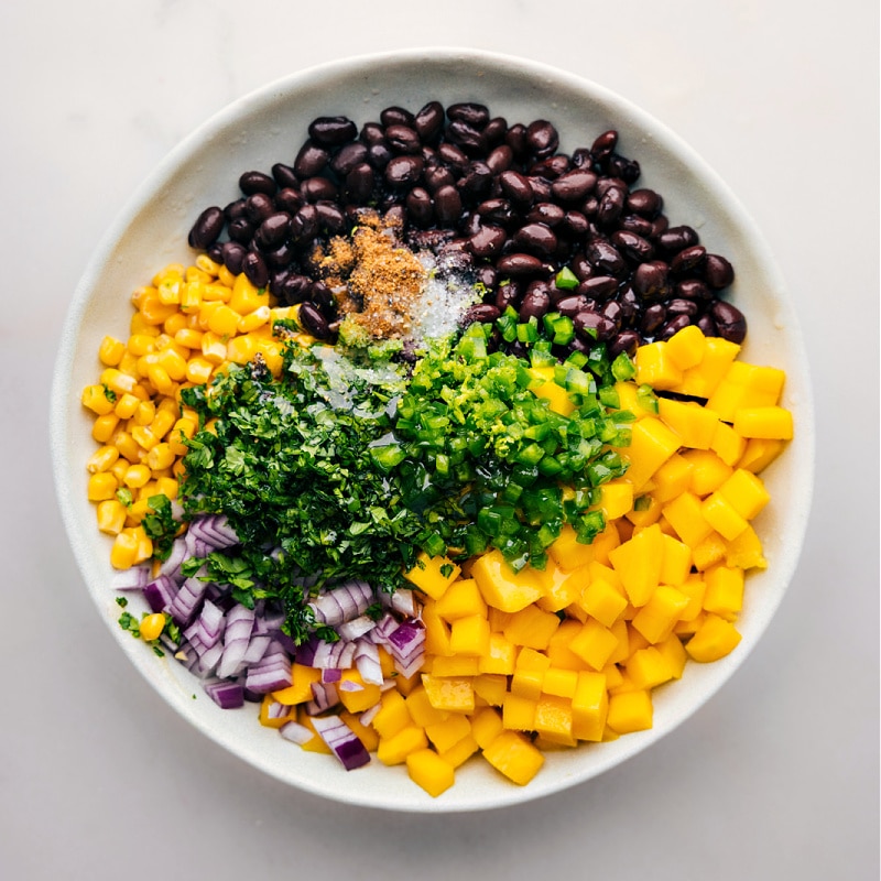 How To Make Mango Black Bean Salsa Mango Black Bean Salsa ingredients all added to a bowl to be mixed together.