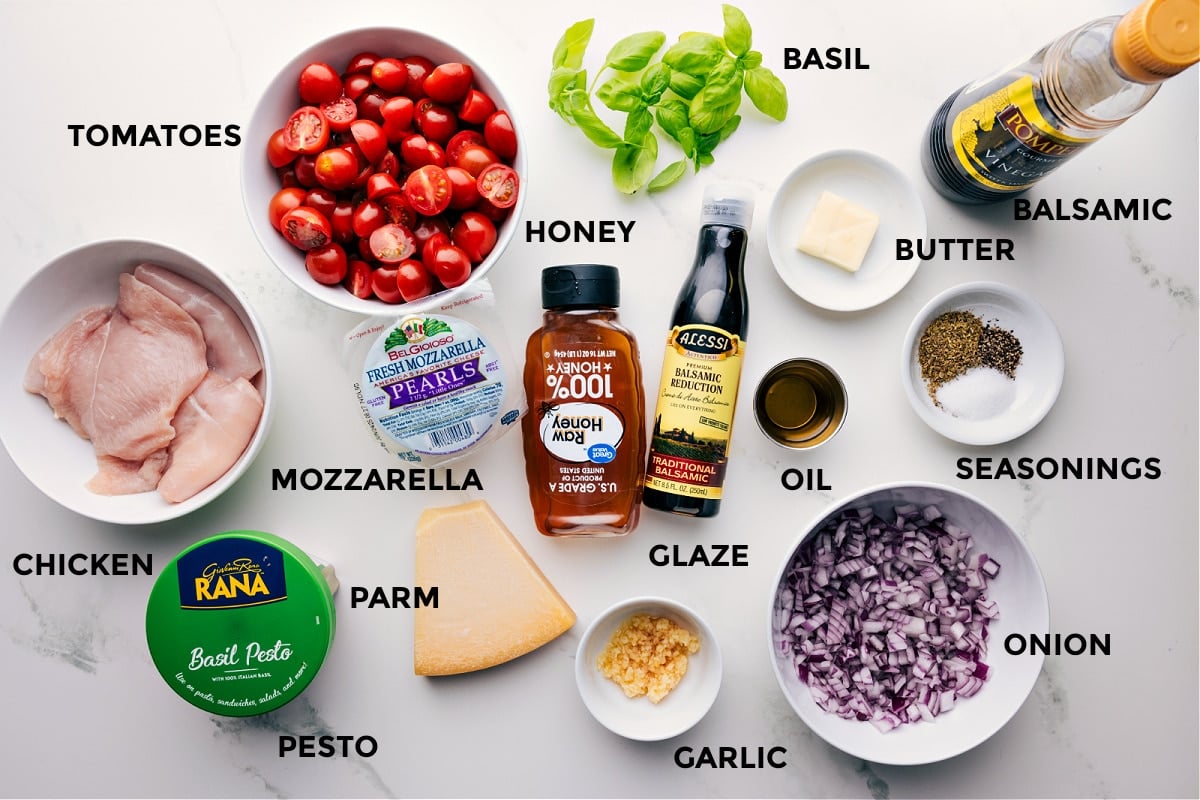 Ingredients In Caprese Chicken Recipe All the ingredients for this recipe are prepped and ready for easy assembly, including basil, meat, balsamic, butter, seasonings, onion, oil, glaze, honey, garlic, Parmesan, mozzarella, pesto, and tomatoes.