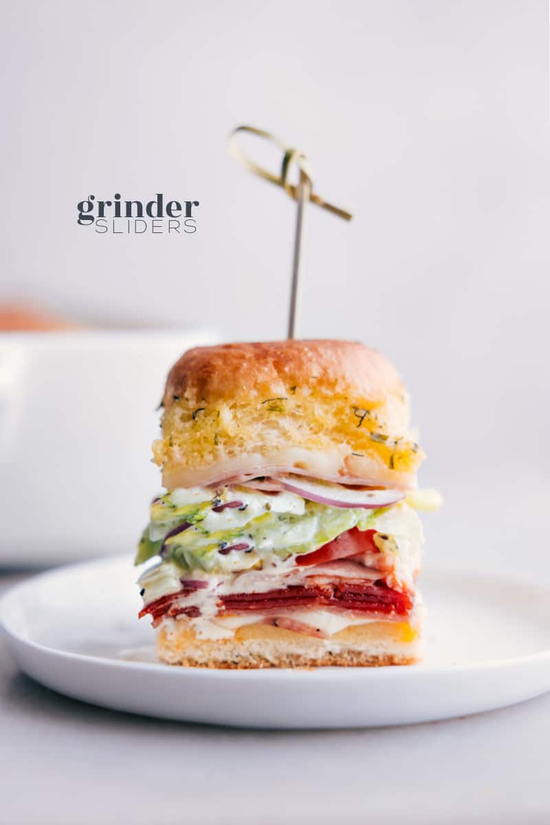 These Grinder Sliders offer bold and robust flavors from the savory combination of salami, pepperoni, and ham complemented by the rich and creamy melted Provolone cheese, all nestled within sweet Hawaiian rolls. The sliders are topped with a fresh and tangy sub slaw, featuring crisp iceberg lettuce, zingy banana peppers, and a sharp, bright dressing, offering a burst of flavors in every bite. Recipe via chelseasmessyapron #lunch #quick #easy #simple #familyfriendly #kidfriendly #comfortfood #turkey #pepperoni #grinder #sliders Image of the Grinder Sliders on a plate ready to be enjoyed