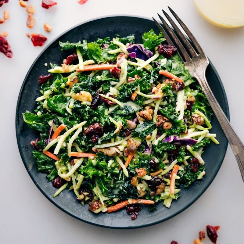 Kale Cranberry Pecan Salad! The tangy, sweet dressing of honey, apple cider vinegar, Dijon mustard, olive oil, and mayonnaise enhances the fresh ingredients. Enjoy this salad as a light standalone meal or pair it with your choice of protein for a heartier dish. Recipe via chelseasmessyapron #healthy #quick #easy #simple #cleaneating #sidedish #kale #cranberry #pecan #salad Up close overhead image of the Kale Cranberry Pecan Salad