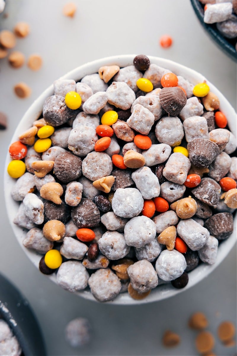 This delicious Peanut Butter Puppy Chow is the snack mix of the century! Think peanut buttery crunchy cereal mixed with sweet, melty chocolate and all covered in powdered sugar. Toss in extras like Reese's minis and peanut butter chips, and you've got yourself a treat that's insanely tasty, addictively crunchy, and utterly irresistible! Recipe via chelseasmessyapron #dessert #best #quick #easy #simple #treat #nobake #snack #chocolatechips #peanutbutter #puppychow Up-close overhead image of the treat ready to be enjoyed