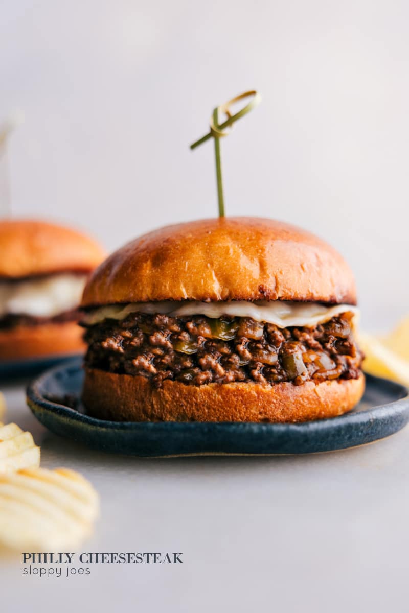 These Philly Cheesesteak Sloppy Joes blend juicy ground beef with a kick of A1 and Worcestershire sauce, a touch of sweetness from ketchup and the melt-in-your-mouth creaminess of provolone cheese, all held together by a buttery toasted brioche bun. It's a fun mash-up of two American faves! Recipe via chelseasmessyapron #dinner #quick #easy #simple #best #familyfriendly #kidfriendly #groundbeef #phillycheesesteak #sloppyjoes Philly Cheesesteak Sloppy joes on a plate.