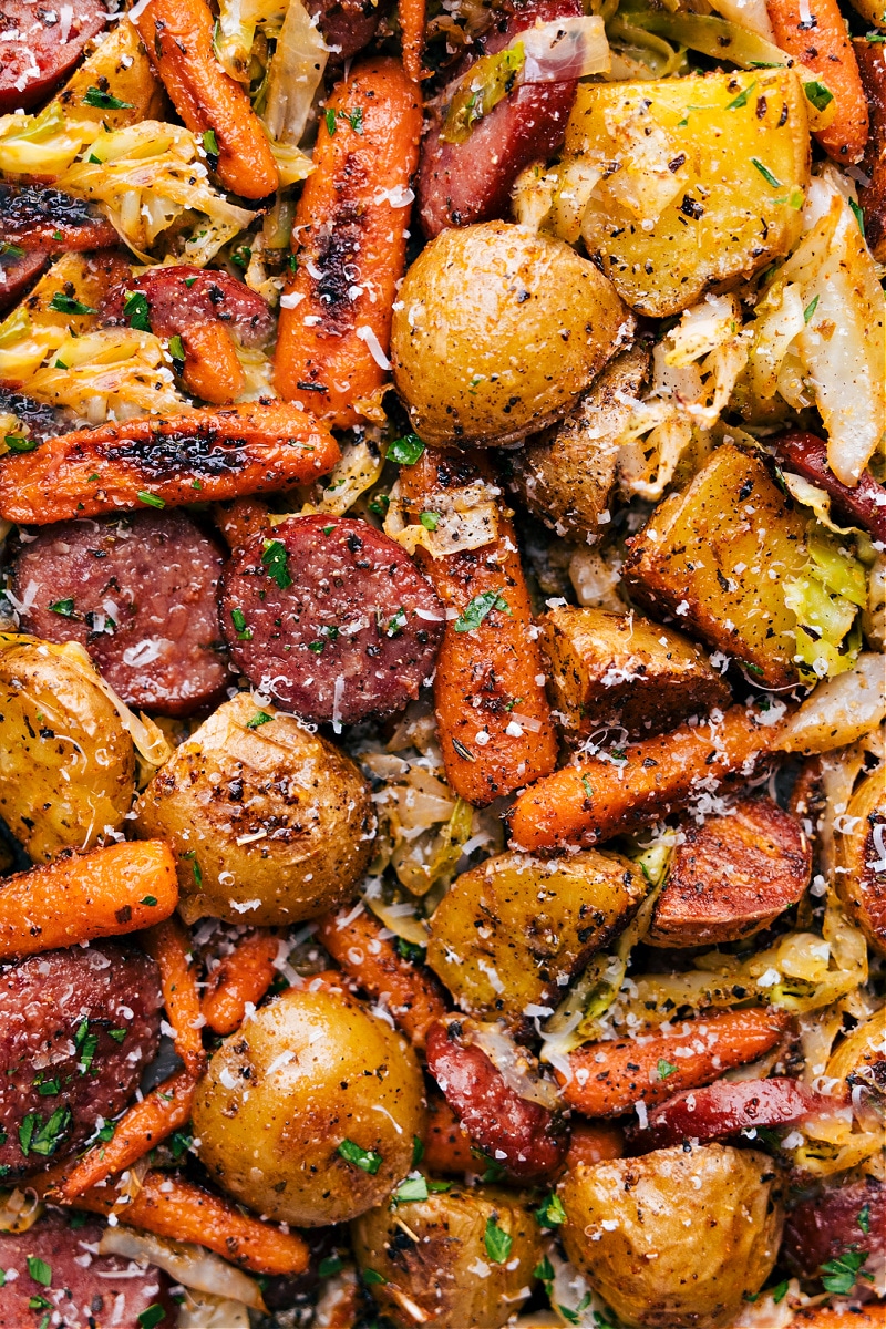 Our favorite Cabbage, Potatoes, and Sausage combines smoky sausage with roasted veggies, all topped off with a hit of Parmesan and a drizzle of the best creamy dijon sauce! It's a hearty and flavorful one-pan wonder that's bursting with flavor and so easy to make! Recipe via chelseasmessyapron #dinner #quick #easy #healthy #onepan #cleaneating #wholefoods #cabbage #potatoes #sausage Overhead image of the dish fresh out of the oven ready to be enjoyed